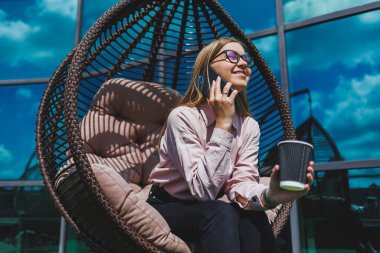 Güneşli bir günde açık havada kahve molası veren gözlüklü neşeli bir iş kadınının portresi. Ofisin arka planında otururken telefonda konuşan başarılı bir kadın yönetici.