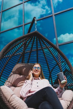 Güneşli bir günde açık havada kahve molası veren gözlüklü neşeli bir iş kadınının portresi. Ofisin arka planında otururken telefonda konuşan başarılı bir kadın yönetici.