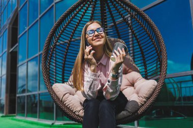 Güneşli bir günde açık havada kahve molası veren gözlüklü neşeli bir iş kadınının portresi. Ofisin arka planında otururken telefonda konuşan başarılı bir kadın yönetici.