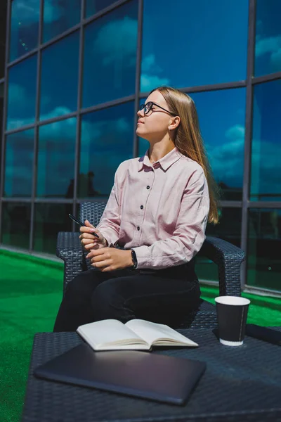 Not defteriyle sokak kafesinde poz veren neşeli bayan öğrenci ders kitabı ve kahve bardağıyla dışarıda gülümseyen başarılı kadın.