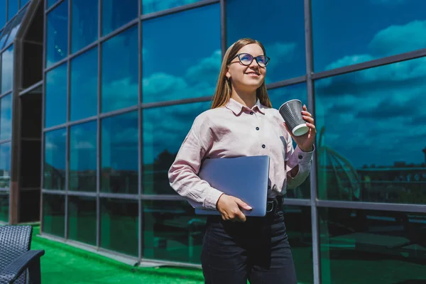 Elinde kahve olan bardaklı bir kadın, gökdelene karşı. Modern bina, finans merkezi, şehir manzarası. Gözlüklü başarılı bir bayan girişimci.