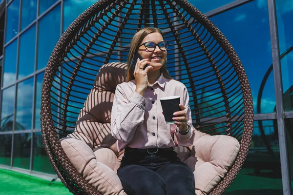 Güneşli bir günde açık havada kahve molası veren gözlüklü neşeli bir iş kadınının portresi. Ofisin arka planında otururken telefonda konuşan başarılı bir kadın yönetici.