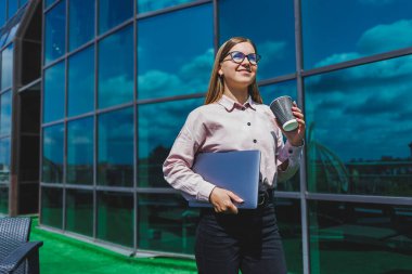 Elinde kahve olan bardaklı bir kadın, gökdelene karşı. Modern bina, finans merkezi, şehir manzarası. Gözlüklü başarılı bir bayan girişimci.