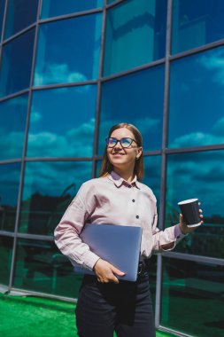 Elinde kahve olan bardaklı bir kadın, gökdelene karşı. Modern bina, finans merkezi, şehir manzarası. Gözlüklü başarılı bir bayan girişimci.