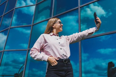 Çekici kadın blogcu elinde modern bir alet tutuyor, düşünceli ve hayalperest görünüyor, cep telefonu tutan genç blogcu, sosyal medyada paylaşım yapma fikrini düşünüyor.