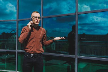 Görme düzeltmesi için klasik gözlüklü mutlu adam cep telefonuyla terasta konuşuyor, gülen blogcu sosyal medya sitesine göz atıyor.