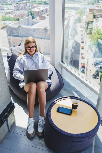 Young millennial woman in classic eye protection glasses connecting to WIFI internet on laptop in coworking space to browse web information on digital netbooks, european woman chatting