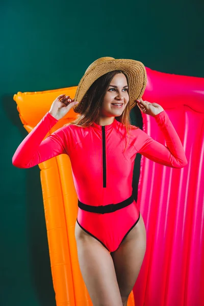 Pembe mayo giymiş mutlu genç bir kadının portresi yeşil arka planda izole edilmiş şişme pembe şilteli gülümseyen bir kız.