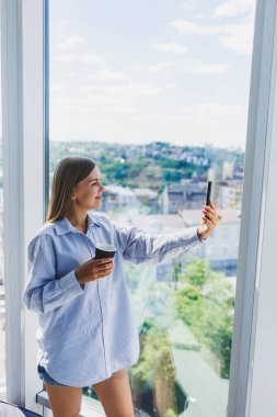 Mutlu kadın kahve içer ve bir kafede pencereden dışarı bakar. Gözlüklü genç bir kız pencerenin yanında duruyor. Eğlence, boş zaman ve boş zaman. Modern serbest yaşam tarzı.