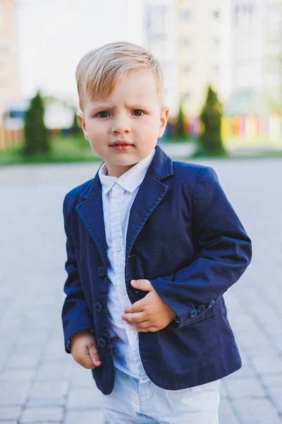 A little boy 2 years old in a shirt and jacket stands on the street. Children\'s classic costume for the holiday. Children\'s fashion.