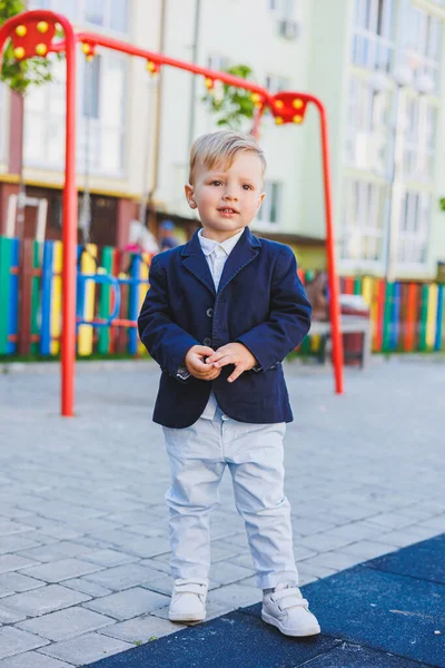 İki yaşında, gömlekli ve ceketli küçük bir çocuk sokakta duruyor. Tatil için klasik çocuk kostümü. Çocuk modası.