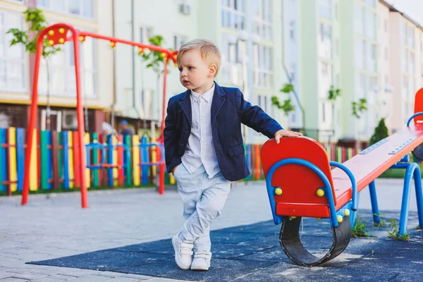 İki yaşında, gömlekli ve ceketli küçük bir çocuk sokakta duruyor. Tatil için klasik çocuk kostümü. Çocuk modası.