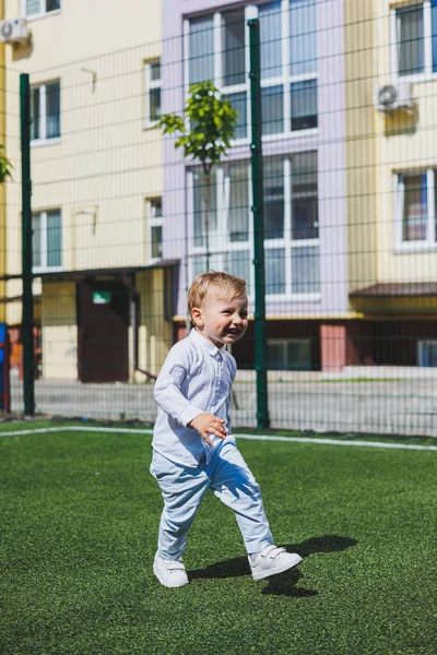 A little boy 2 years old in a shirt and trousers runs and laughs. A child on a sunny day rejoices and smiles.