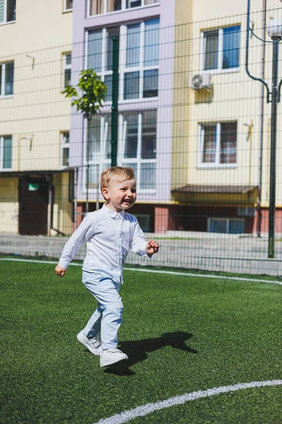 A little boy 2 years old in a shirt and trousers runs and laughs. A child on a sunny day rejoices and smiles.
