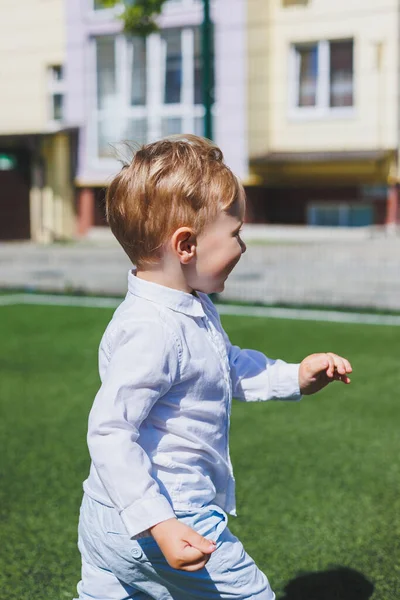 2 yaşında gömlekli ve pantolonlu bir çocuk koşuyor ve gülüyor. Güneşli bir günde bir çocuk sevinir ve gülümser..