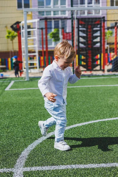 The child runs in the park. A boy in a white shirt and trousers. Green lawn or field. Mowed lawn. Walk and play in the forest. Active sports.