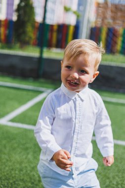 Çocuk parkta koşar. Beyaz gömlekli ve pantolonlu bir çocuk. Yeşil çimen ya da tarla. Çimleri biçtim. Ormanda yürü ve oyna. Etkin sporlar.