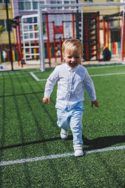 Çocuk parkta koşar. Beyaz gömlekli ve pantolonlu bir çocuk. Yeşil çimen ya da tarla. Çimleri biçtim. Ormanda yürü ve oyna. Etkin sporlar.