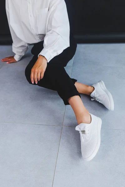 Attractive woman in a white shirt and black trousers, white sneakers with genuine leather on her feet. Summer female casual fashion.