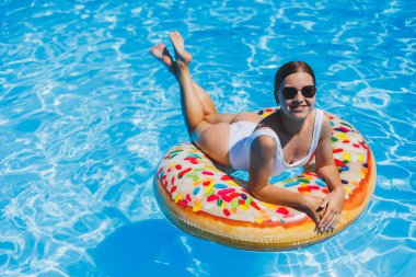 Havuzda dinlen. Mayolu, güneş gözlüklü ve mavi suda yüzen şişme lastik yüzüklü mutlu genç bir kadın. Spa tatil merkezinde yaz tatili