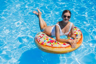 Havuzda dinlen. Mayolu, güneş gözlüklü ve mavi suda yüzen şişme lastik yüzüklü mutlu genç bir kadın. Spa tatil merkezinde yaz tatili