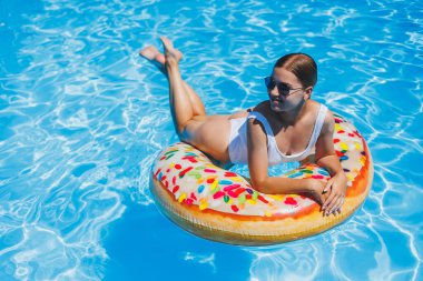 Havuzda dinlen. Mayolu, güneş gözlüklü ve mavi suda yüzen şişme lastik yüzüklü mutlu genç bir kadın. Spa tatil merkezinde yaz tatili