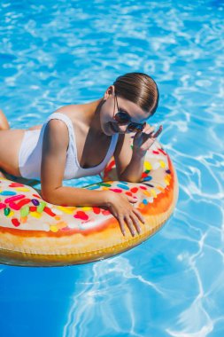 Havuzda dinlen. Mayolu, güneş gözlüklü ve mavi suda yüzen şişme lastik yüzüklü mutlu genç bir kadın. Spa tatil merkezinde yaz tatili