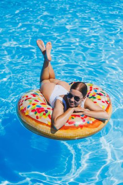 Havuzda dinlen. Mayolu, güneş gözlüklü ve mavi suda yüzen şişme lastik yüzüklü mutlu genç bir kadın. Spa tatil merkezinde yaz tatili
