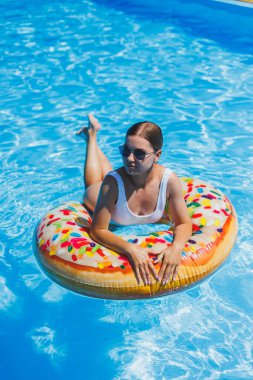 Havuzda dinlen. Mayolu, güneş gözlüklü ve mavi suda yüzen şişme lastik yüzüklü mutlu genç bir kadın. Spa tatil merkezinde yaz tatili