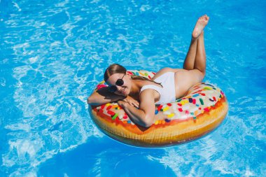 Havuzda dinlen. Mayolu, güneş gözlüklü ve mavi suda yüzen şişme lastik yüzüklü mutlu genç bir kadın. Spa tatil merkezinde yaz tatili