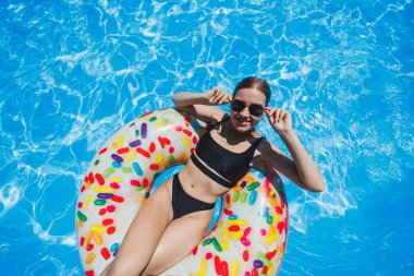 Havuzda güneş gözlüklü güzel bir kadın siyah bir mayo içinde şişme bir yüzükte yüzüyor, yaz fotoğrafı, yüzme fotoğrafı, yaz kadını fotoğrafları.