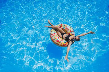Havuzda güneş gözlüklü güzel bir kadın siyah bir mayo içinde şişme bir yüzükte yüzüyor, yaz fotoğrafı, yüzme fotoğrafı, yaz kadını fotoğrafları.