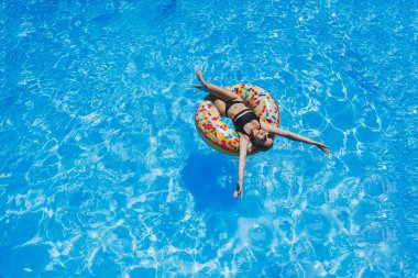 Havuzda güneş gözlüklü güzel bir kadın siyah bir mayo içinde şişme bir yüzükte yüzüyor, yaz fotoğrafı, yüzme fotoğrafı, yaz kadını fotoğrafları.