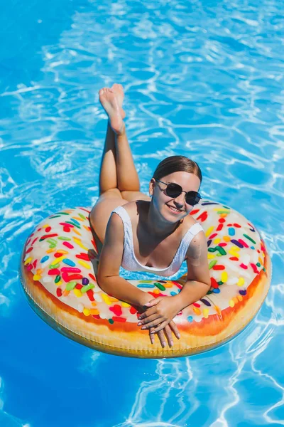 Havuzda dinlen. Mayolu, güneş gözlüklü ve mavi suda yüzen şişme lastik yüzüklü mutlu genç bir kadın. Spa tatil merkezinde yaz tatili
