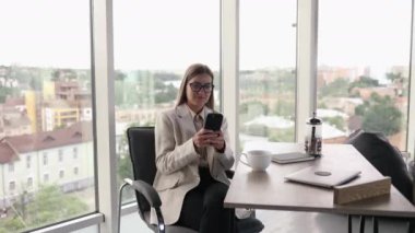 Gözlüklü güzel bir bayan parlak bir ofiste çalışıyor ve dizüstü bilgisayarda çay içiyor. Çekici, uzun saçlı, gözlüklü bir kadın telefonda konuşuyor.