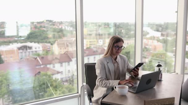 戴眼镜的年轻漂亮女人在明亮的办公室工作 在笔记本电脑边喝茶 迷人的长发女士 戴着眼镜在电话里聊天 — 图库视频影像