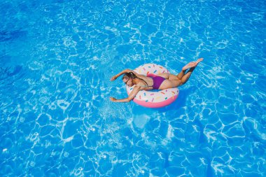 Havuzda güneş gözlüklü sıska bir kadın parlak bir mayo içinde şişme bir yüzme yüzüğüyle, yaz fotoğrafı, yüzme fotoğrafı, yazlık kadın fotoğrafları. Plaj modası