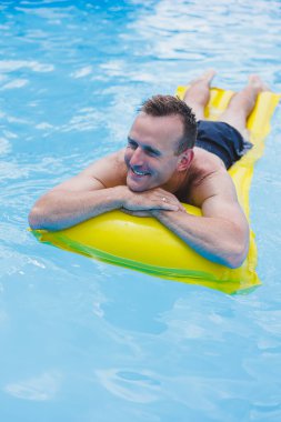 Handsome man in swimming shorts with an inflatable yellow mattress in the pool. Summer vacation in the hotel