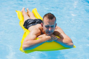 Handsome man in swimming shorts with an inflatable yellow mattress in the pool. Summer vacation in the hotel