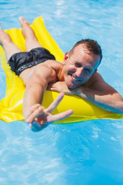 Handsome man in swimming shorts with an inflatable yellow mattress in the pool. Summer vacation in the hotel