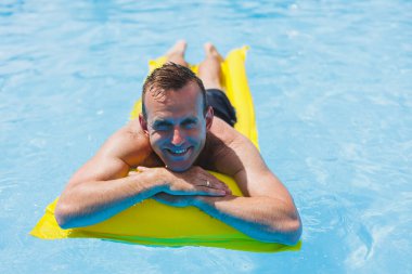 Handsome man in swimming shorts with an inflatable yellow mattress in the pool. Summer vacation in the hotel