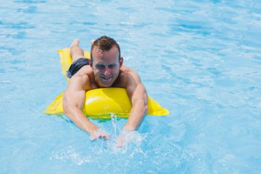 Handsome man in swimming shorts with an inflatable yellow mattress in the pool. Summer vacation in the hotel