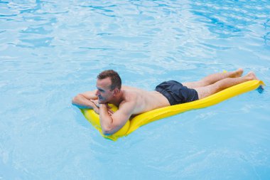 Handsome man in swimming shorts with an inflatable yellow mattress in the pool. Summer vacation in the hotel