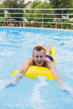 Handsome man in swimming shorts with an inflatable yellow mattress in the pool. Summer vacation in the hotel