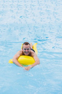 Handsome man in swimming shorts with an inflatable yellow mattress in the pool. Summer vacation in the hotel