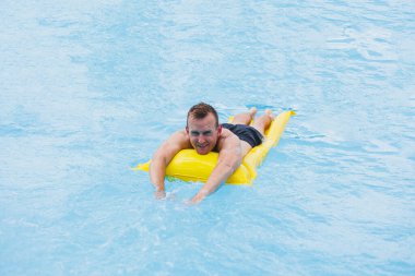 Handsome man in swimming shorts with an inflatable yellow mattress in the pool. Summer vacation in the hotel