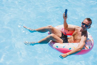 Çekici bir adam havuzda şişme bir yüzüğün üzerinde dinleniyor. Havuzda bir adam telefonda konuşuyordu. tatil ve boş zaman kavramı