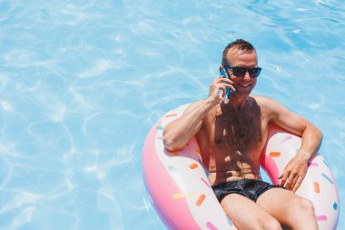 Çekici bir adam havuzda şişme bir yüzüğün üzerinde dinleniyor. Havuzda bir adam telefonda konuşuyordu. tatil ve boş zaman kavramı