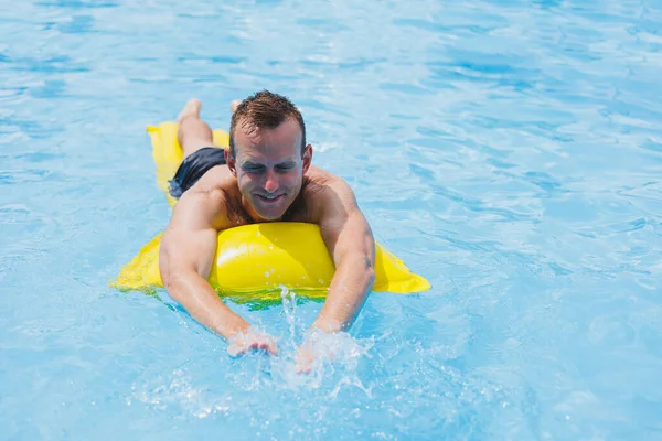 Handsome man in swimming shorts with an inflatable yellow mattress in the pool. Summer vacation in the hotel