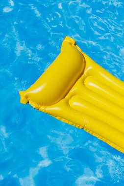 Sarı bir şişme yatak boş bir mavi su havuzunda yüzer. Yaz tatili kavramı